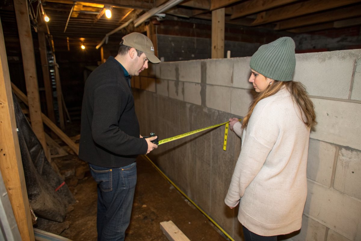Two people measuring a water line on a block basement wall