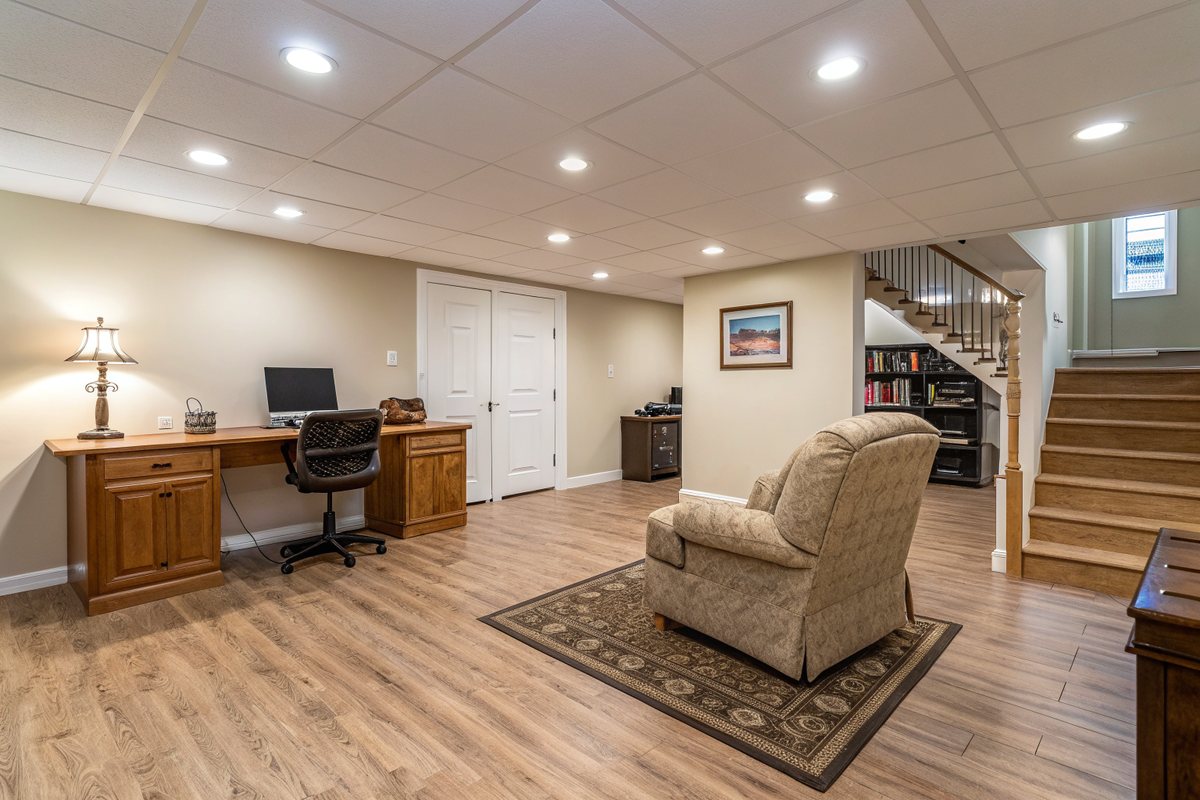 A bright finished basement office and lounge with wood-look flooring and an armchair